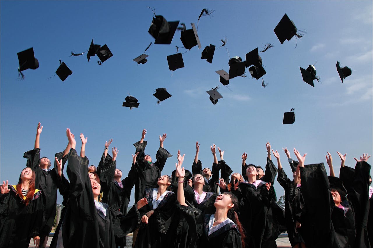 home-hero Group of graduates celebrating by throwing caps in the air during a sunny day.